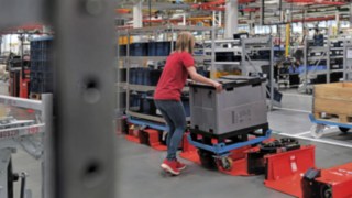 Bedienerin belädt einen Routenzuganhänger mit einem Trolley in Halbgrösse