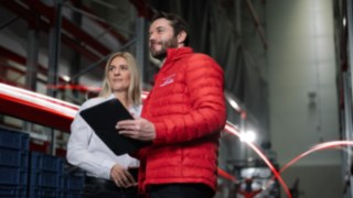 Ein Mann in roter Jacke von Linde MH und eine Frau mit weissem Hemd stehen in einem Warenhaus und schauen in die Ferne.