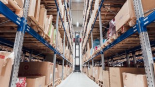 Un VNA soulève une palette dans un entrepôt en hauteur, entouré de rayonnages garnis de cartons