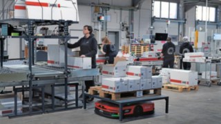 Automatisiertes Plattformfahrzeug C-MATIC von Linde MH inmitten einer Gruppe von Lager-Mitarbeiterinnen bei ABS Safety.