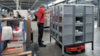 Mitarbeiter von ABS Safety greift Bauteile aus einem Regal, dass der C-MATIC von Linde MH zu ihm bewegt hat.