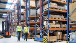 Mitarbeiter von Yanmar Compact Equipment Europe im von Linde Material Handling geplanten Logistikzentrum. Mitarbeiter von Yanmar Compact Equipment Europe laufen durch das neue Logistikzentrum, das von Linde Material Handling geplant wurde.