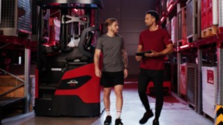 Zwei Personen in Sportkleidung stehen vor einem Linde MH-Schubmaststapler Ri16; eine davon hält ein Tablet in der Hand.