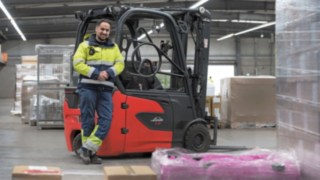 Linde Mitarbeiter lehnt an einem Elektrostapler in einer Lagerhalle