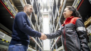 Technicienne de service Linde et client se serrant la main dans un entrepôt à hauts rayonnages.
